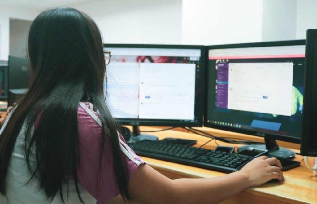 Woman facing two computer monitors.