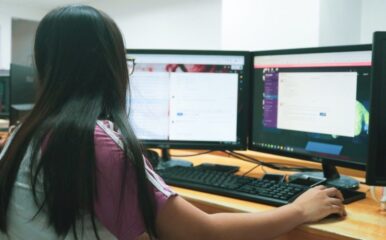 Woman facing two computer monitors.